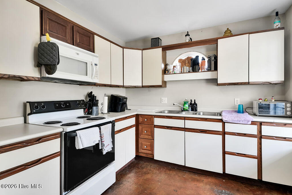 Kitchen with white and dark wood cabinets, electric range, microwave, and stainless-steel sink.