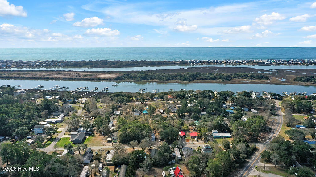 Aerial coastal neighborhood with homes, marshland, waterway, and ocean horizon.