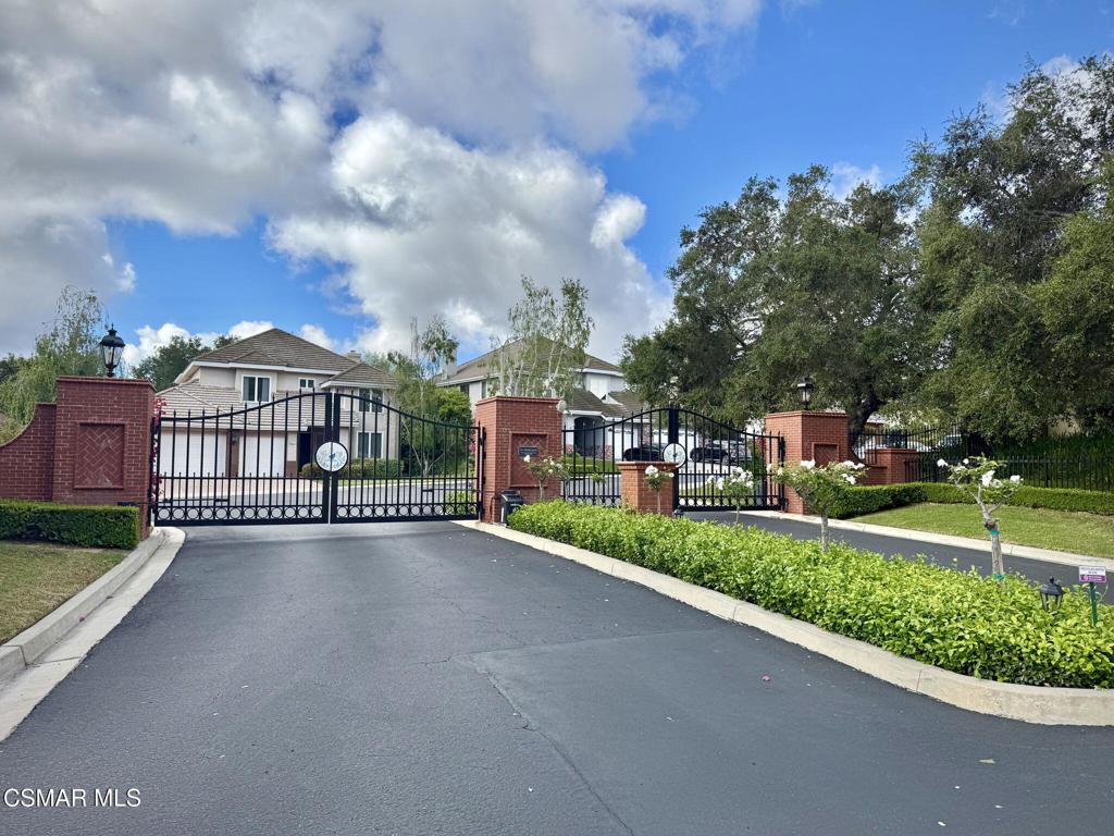 Gated residential entrance with brick pillars, iron gates, and homes beyond.