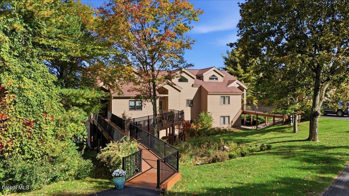Beige multi-level home with elevated decks and a railed wooden walkway among autumn trees.