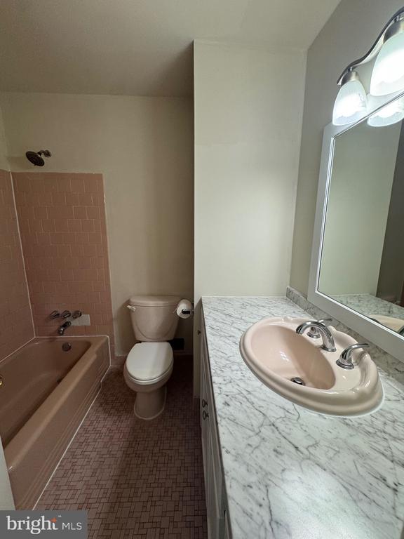 Bathroom with a pink tub and shower tile beside a marble-pattern vanity.