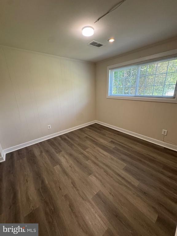 Empty room with beige paneled walls, dark wood-look flooring, and a wide window with blinds.