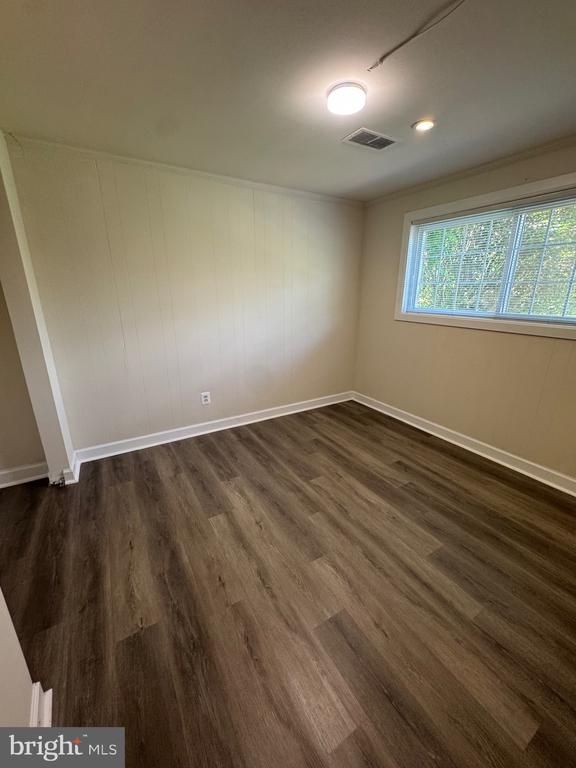 Vacant room with brown plank flooring and a wide window with blinds.