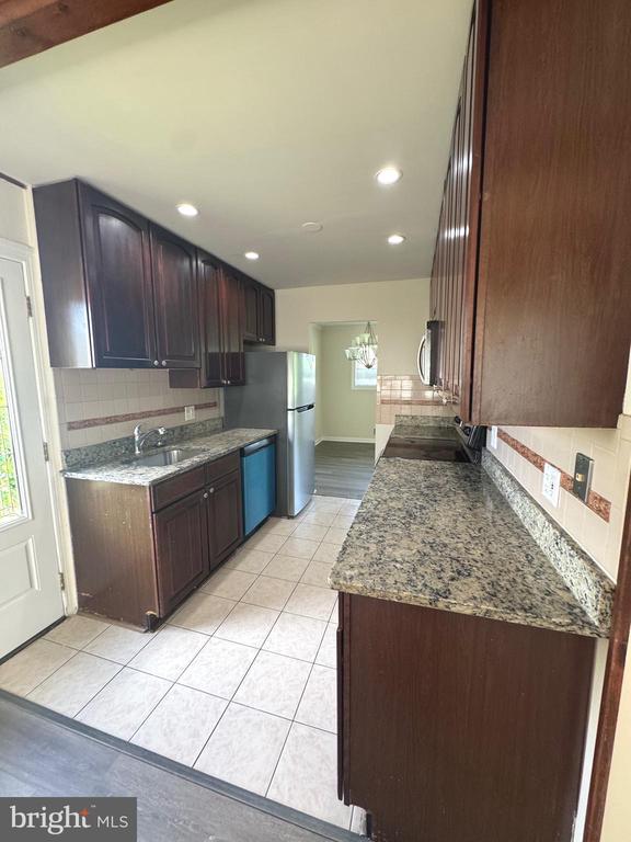Galley kitchen with dark wood cabinets, speckled stone counters, and stainless steel appliances.