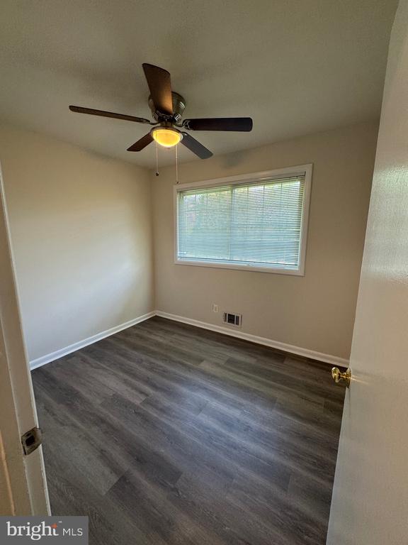 Empty bedroom with gray flooring, window blinds, and a ceiling fan.