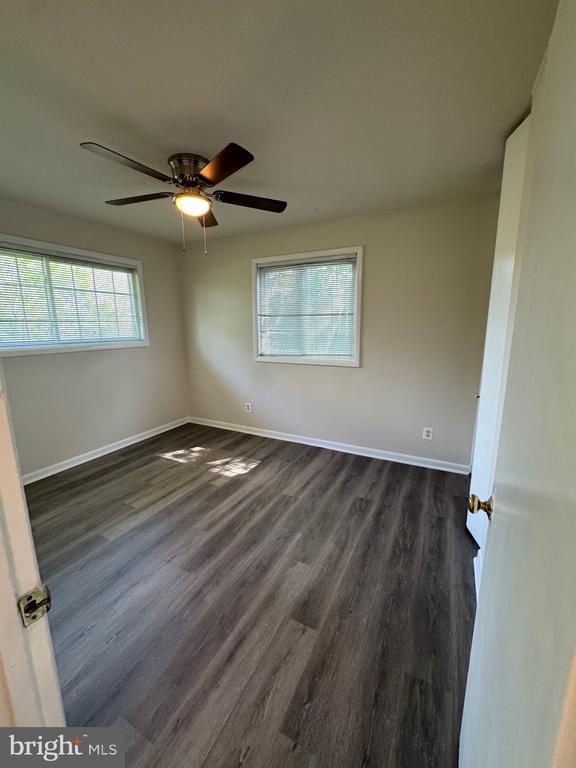 Empty room with two windows, a ceiling fan, and dark wood-look flooring.