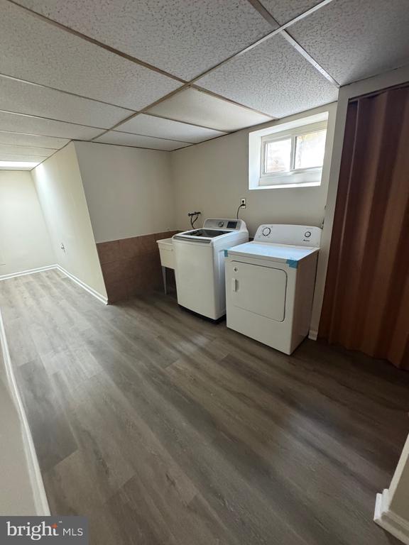Basement laundry room with a top-load washer and dryer, gray plank flooring, and a small high window.