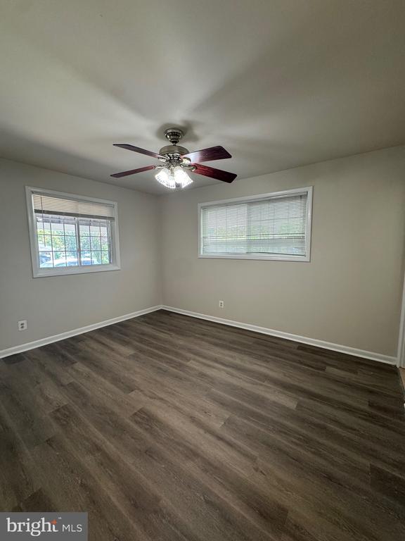 Empty bedroom with dark flooring, two windows, and a ceiling fan with lights