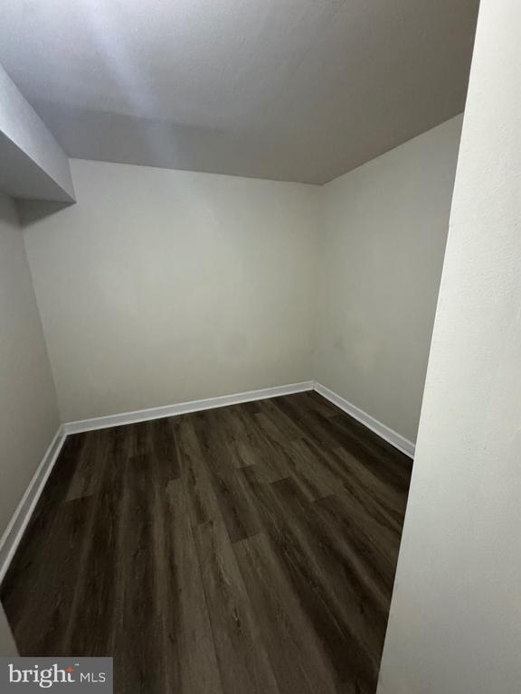 Empty small room with dark wood-look flooring, white walls, and a low angled ceiling.