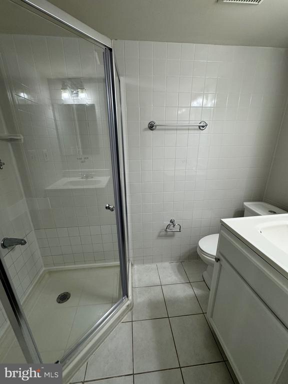 Bathroom with a glass-enclosed shower, white tile, toilet, and vanity.