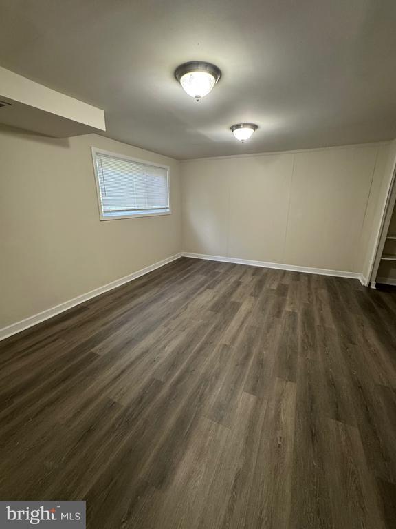 Empty room with dark plank flooring, beige walls, a small window, and two ceiling lights.