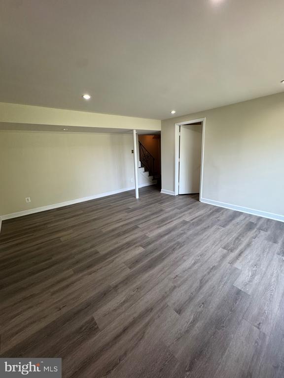 Vacant interior room with gray wood-look flooring, recessed lights, and an open staircase nearby.