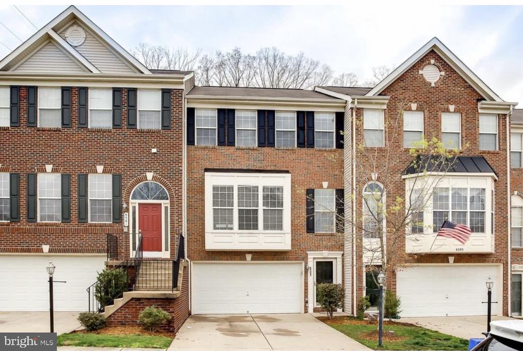 Red-brick townhouse with a white garage, bay window, and American flag.