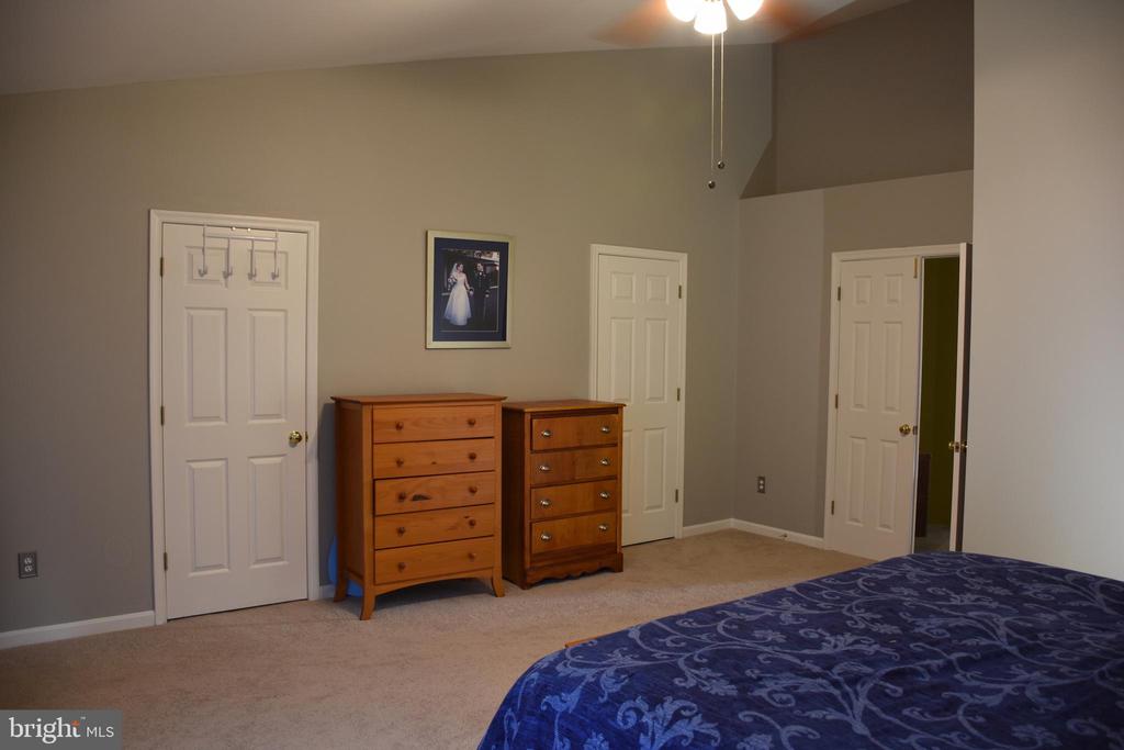 Bedroom with blue patterned bedding, two wooden dressers, and three white doors.