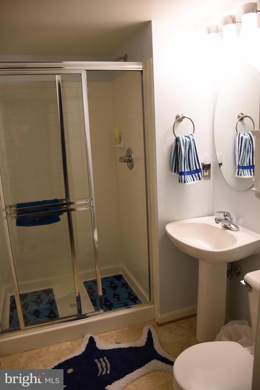 Bathroom with a glass shower, pedestal sink, and blue striped towels.