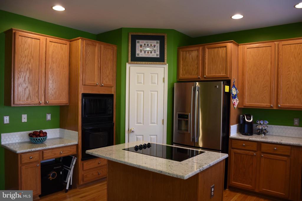 Kitchen with oak cabinets, green walls, and a granite-topped island with cooktop.