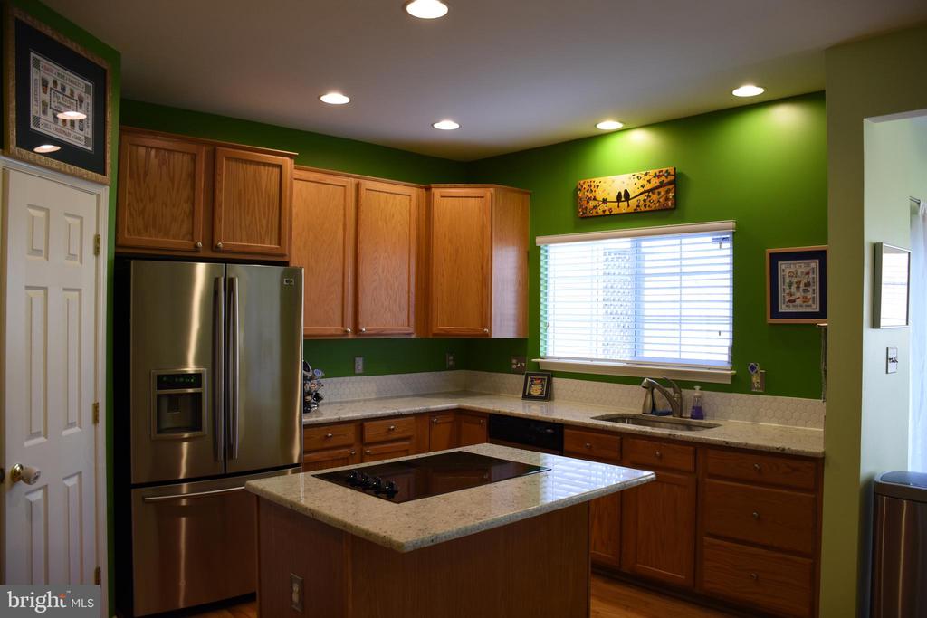 Kitchen with wood cabinetry, granite island and countertops, stainless steel refrigerator, and green walls.
