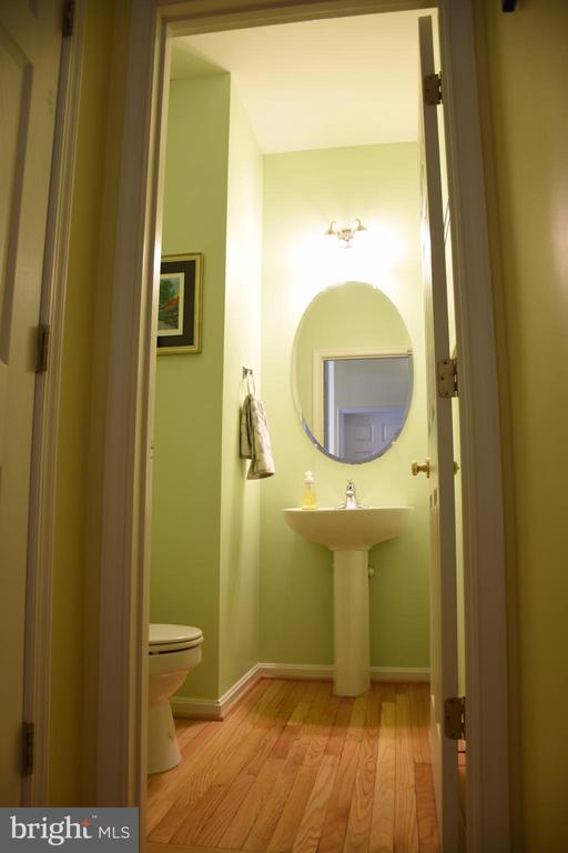 Powder room with a pedestal sink, oval mirror, partially visible toilet, and hardwood floor.