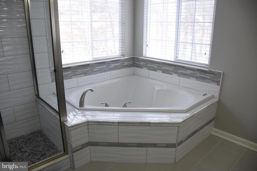 Bathroom with a large corner soaking tub beneath two windows and a glass-enclosed shower.