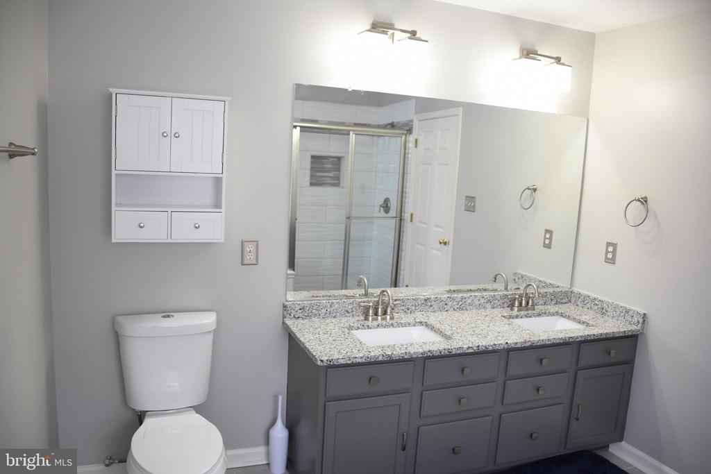 Bathroom with a gray double vanity, speckled granite countertop, and glass-enclosed tiled shower.