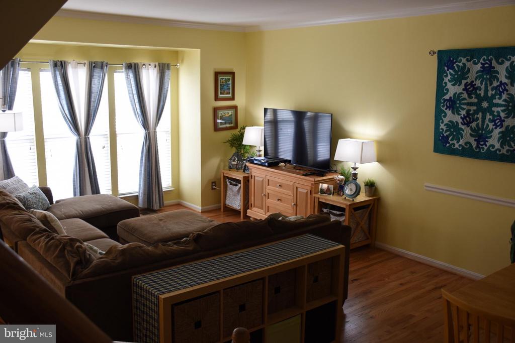 Living room with a brown sectional, hardwood floors, and tall curtained windows.
