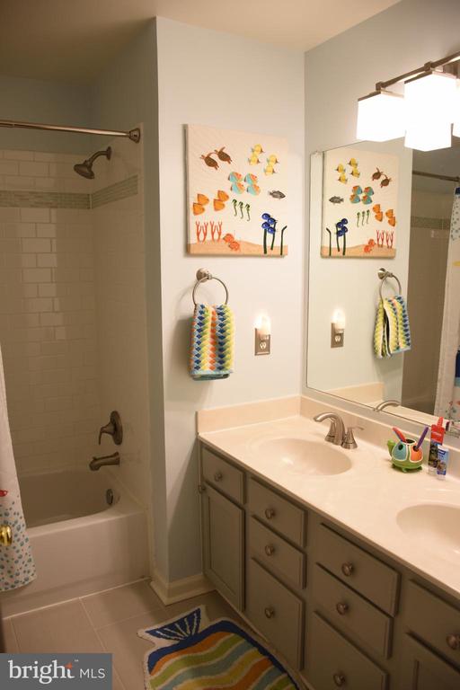 Bathroom with a tiled tub-shower, double-sink vanity, colorful sea-creature artwork, and patterned towels.