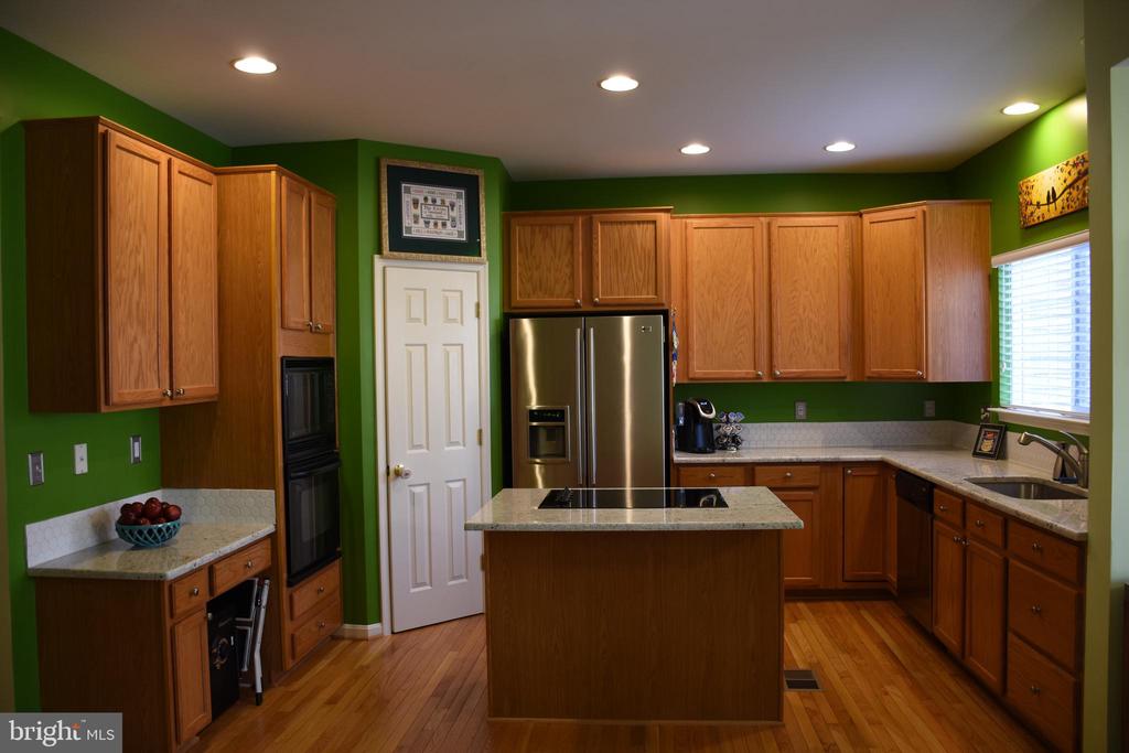 Kitchen with green walls, wood cabinetry, stainless steel appliances, and a central cooktop island.