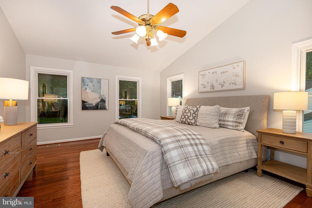 Bedroom with gray plaid bedding, a gray upholstered headboard, hardwood floors, and a wooden ceiling fan.