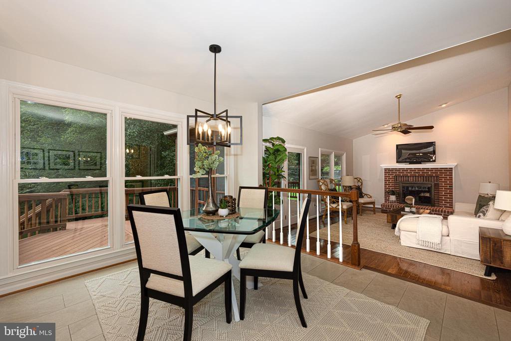 Dining and living room with a glass table, deck-facing windows, and a brick fireplace.
