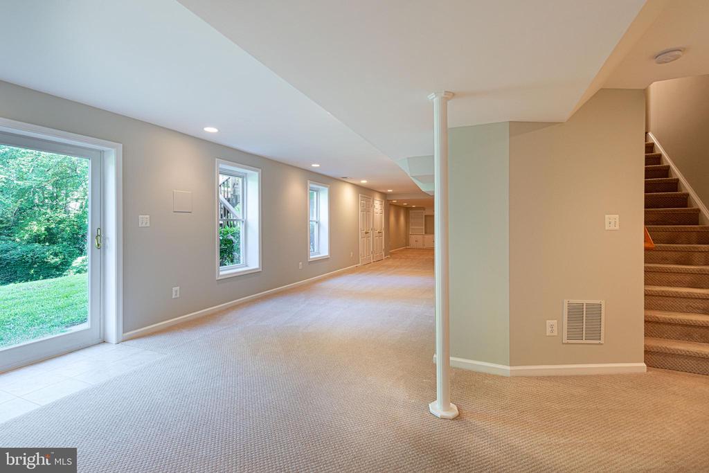 Unfurnished basement recreation room with beige carpet, windows, a sliding glass door, and stairs.