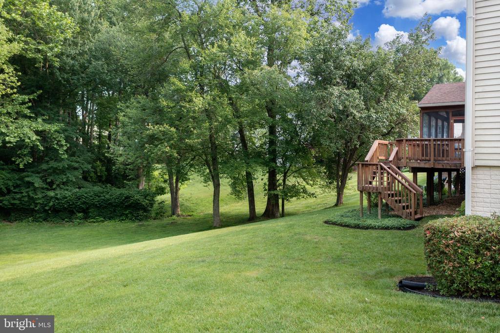 Sloping grassy backyard with mature trees and a raised wooden deck beside the home.