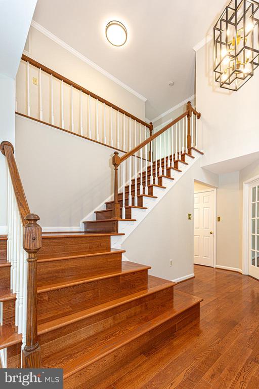 Two-story entryway with a polished hardwood staircase, white balusters, and a geometric chandelier.