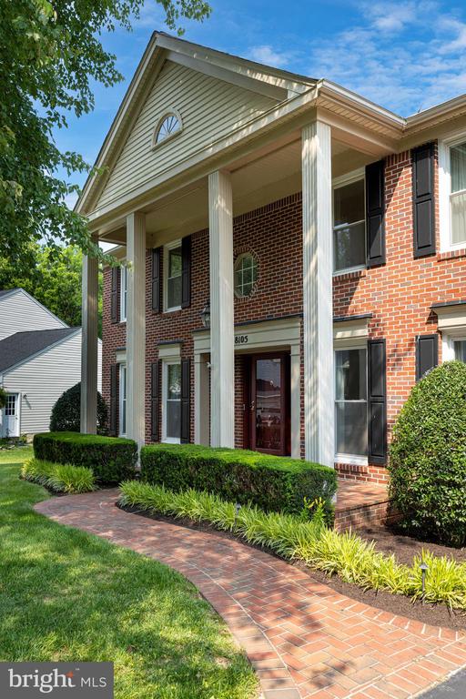 Red-brick house with tall white columns and a curved brick walkway through landscaped front gardens.