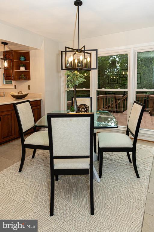 Dining area with a glass-top table and large windows overlooking a deck and trees.