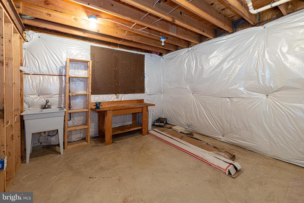 Unfinished basement workshop with plastic-covered walls, a utility sink, and wooden workbench.