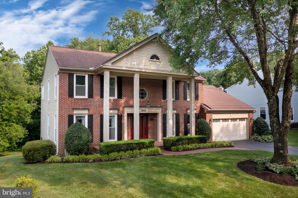 Two-story brick house with a columned entry, attached garage, and landscaped lawn.