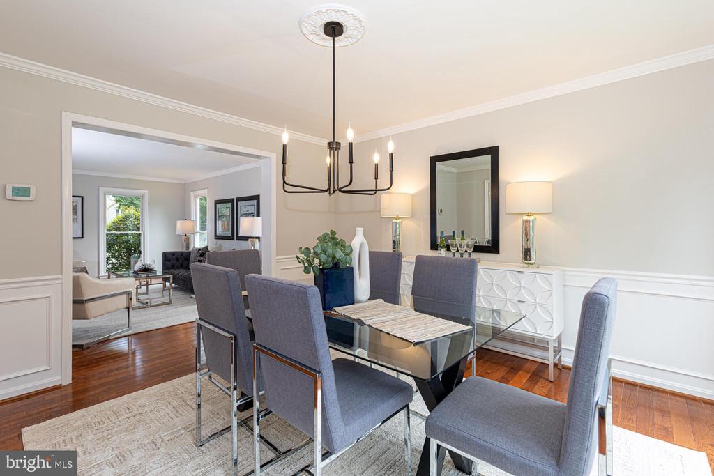 Dining room with a glass-top table and gray chairs, opening onto a furnished living room.