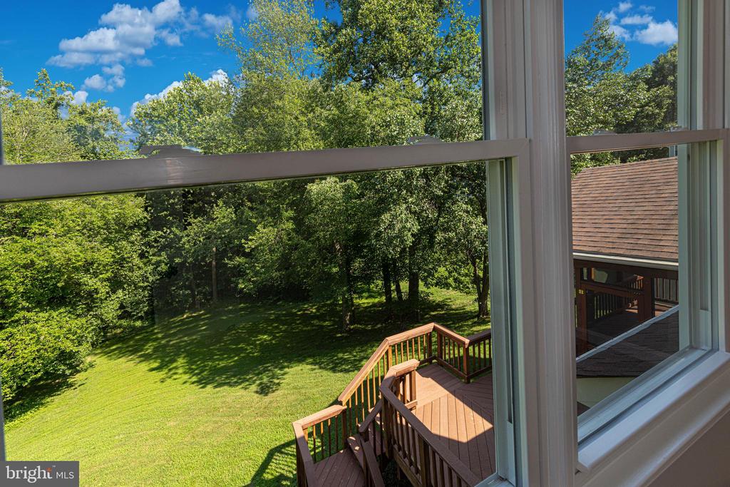 Wooded backyard and green lawn viewed through a window, with a raised wooden deck below.