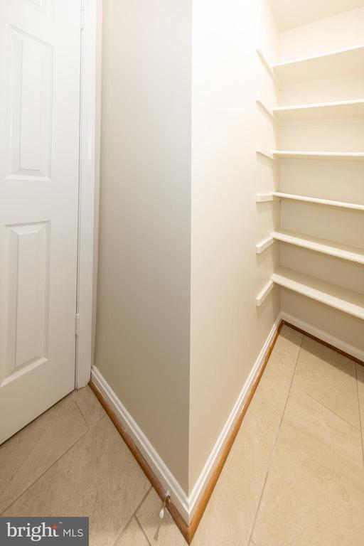 Walk-in pantry with white shelves, a paneled door, and beige tile floor.