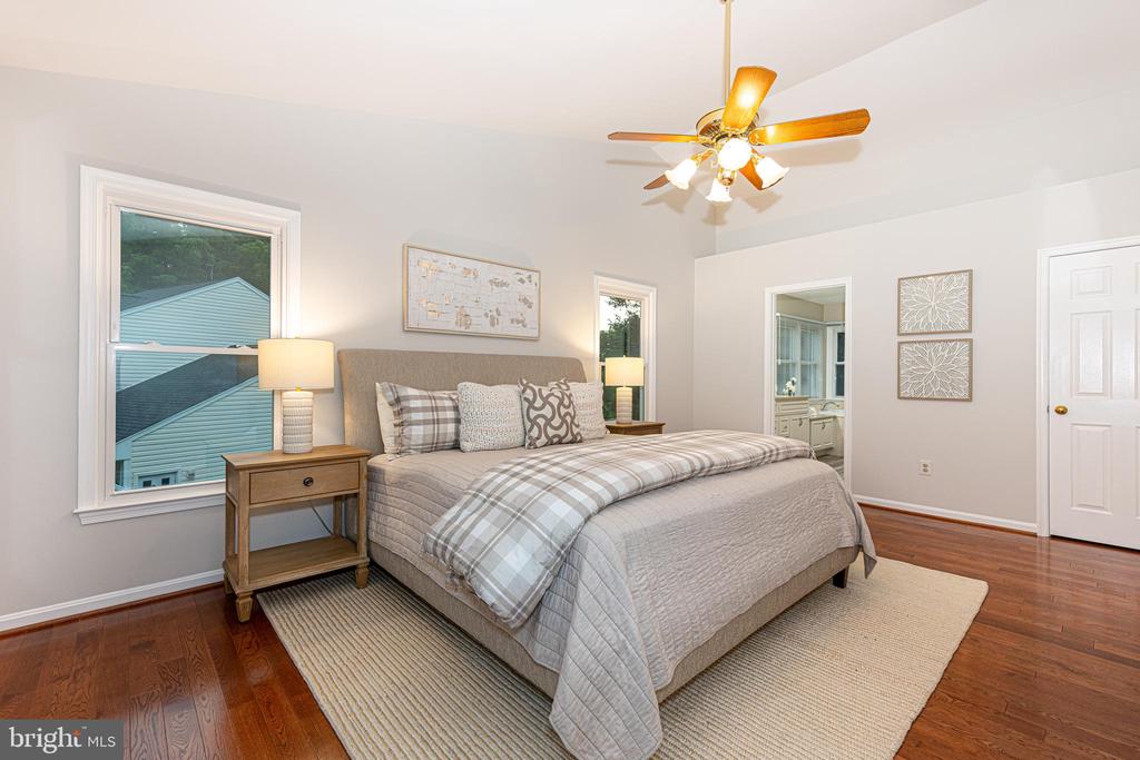 Staged bedroom with gray plaid bedding, wood nightstands, a ceiling fan, and hardwood floors.