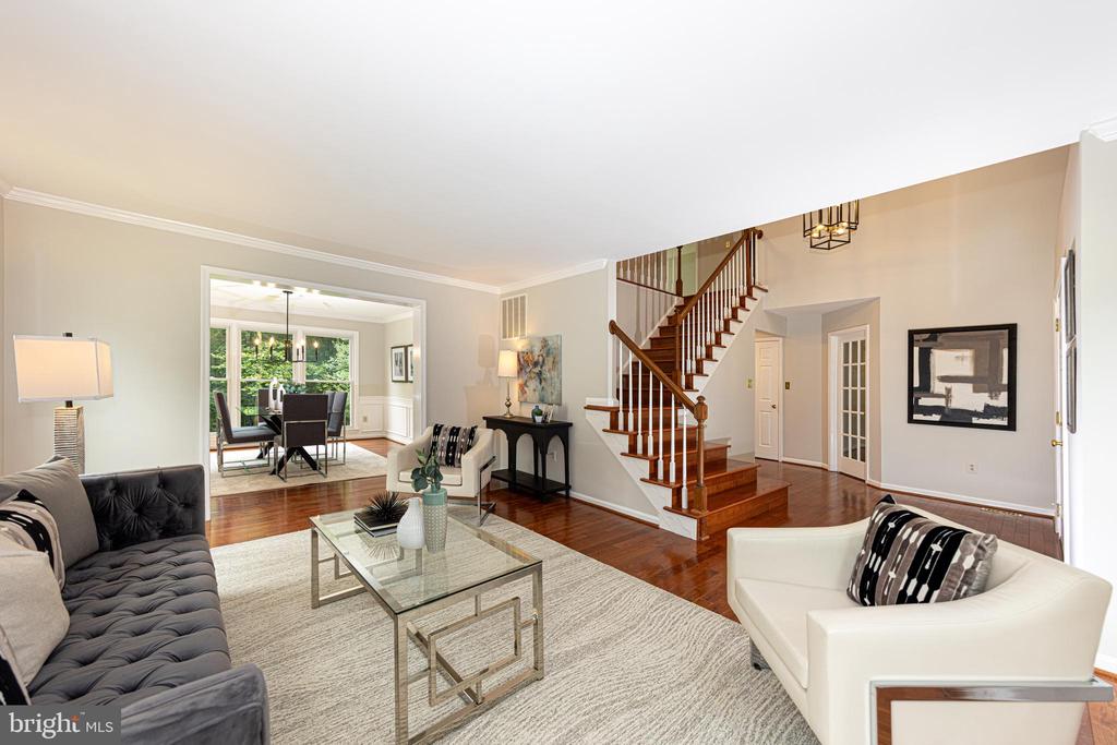 Staged living room with hardwood floors, a glass coffee table, and a prominent wood staircase.