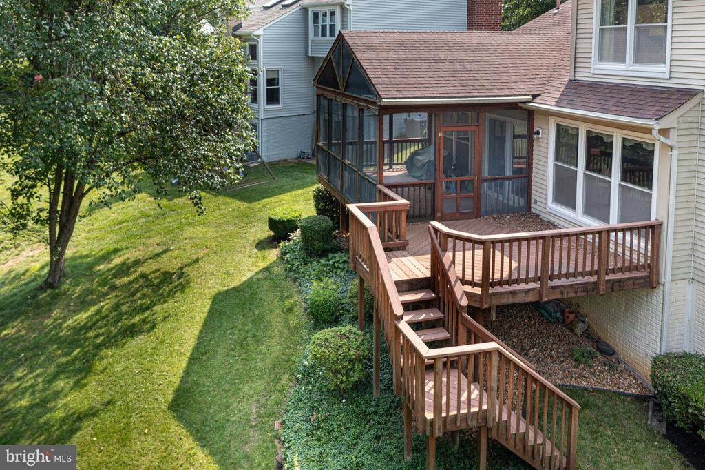 Rear of a house with a raised wooden deck, screened porch, and tree-shaded lawn.
