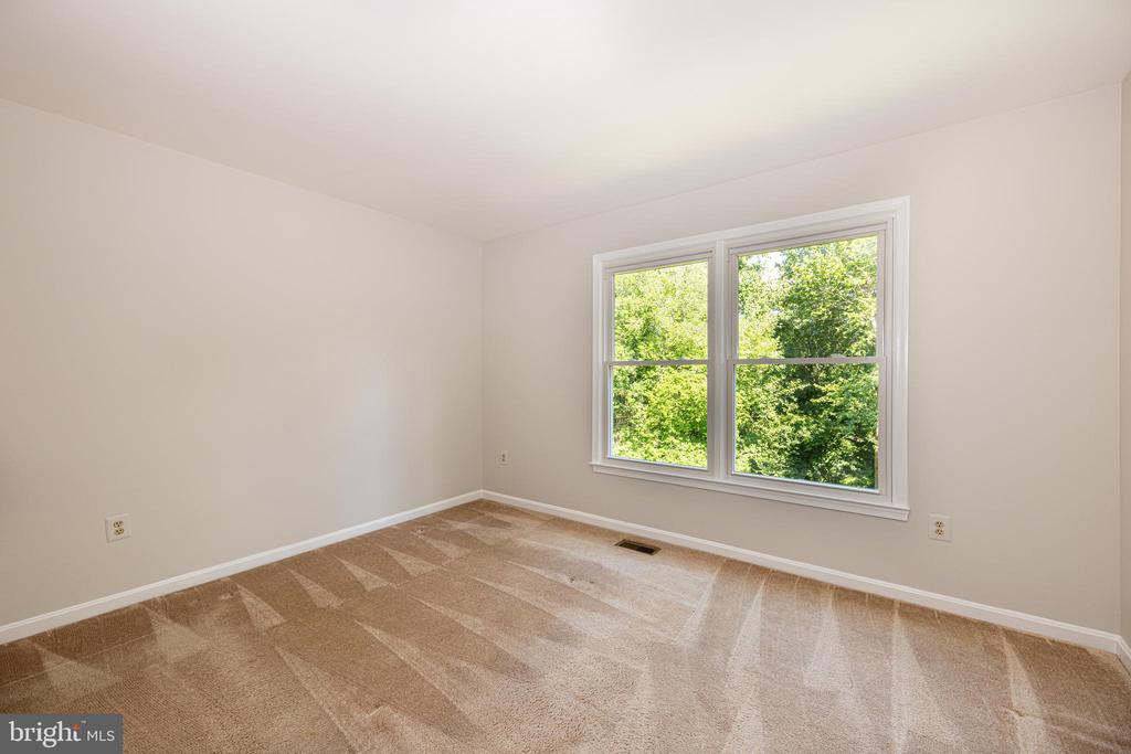 Empty bedroom with tan carpet and a large window overlooking leafy trees.