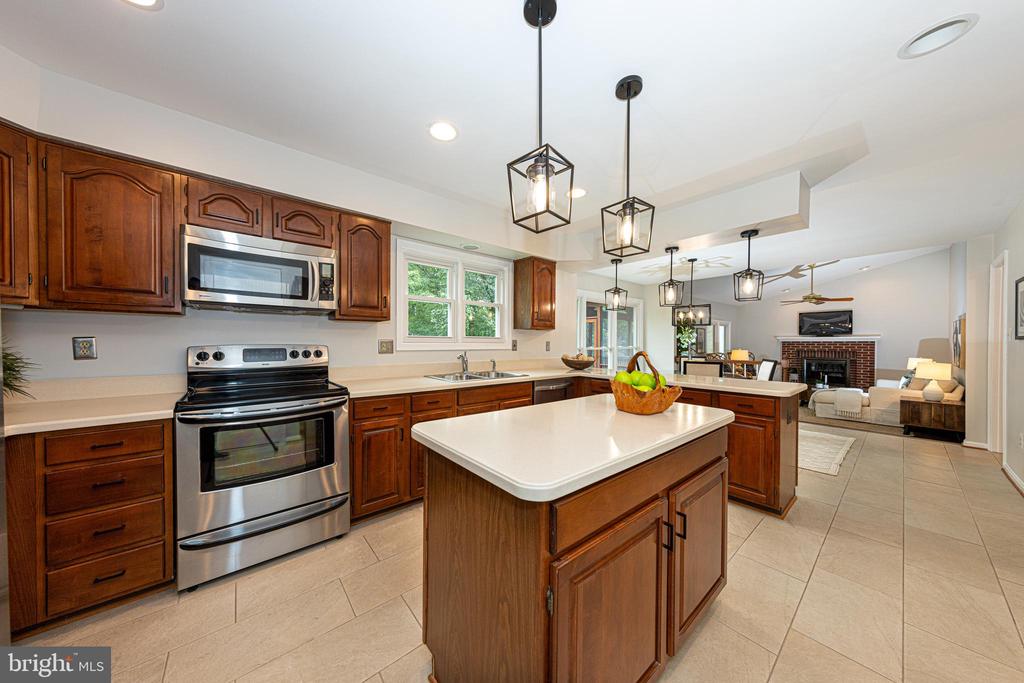 Kitchen with dark wood cabinetry, stainless steel appliances, and a large island opening to a living room.