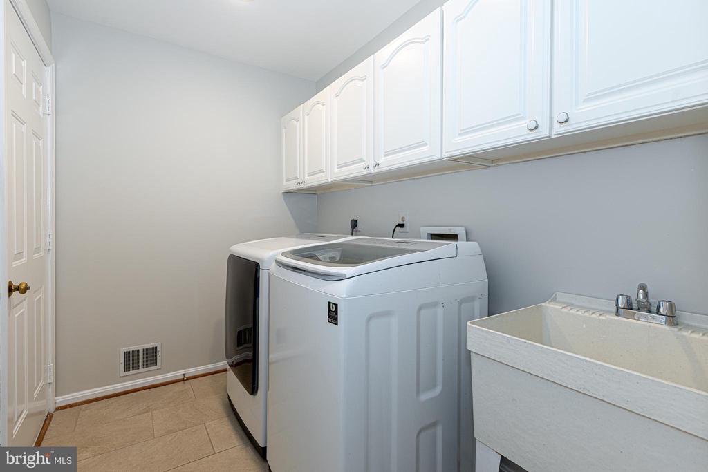 Laundry room with washer and dryer, white cabinets, and a deep utility sink.
