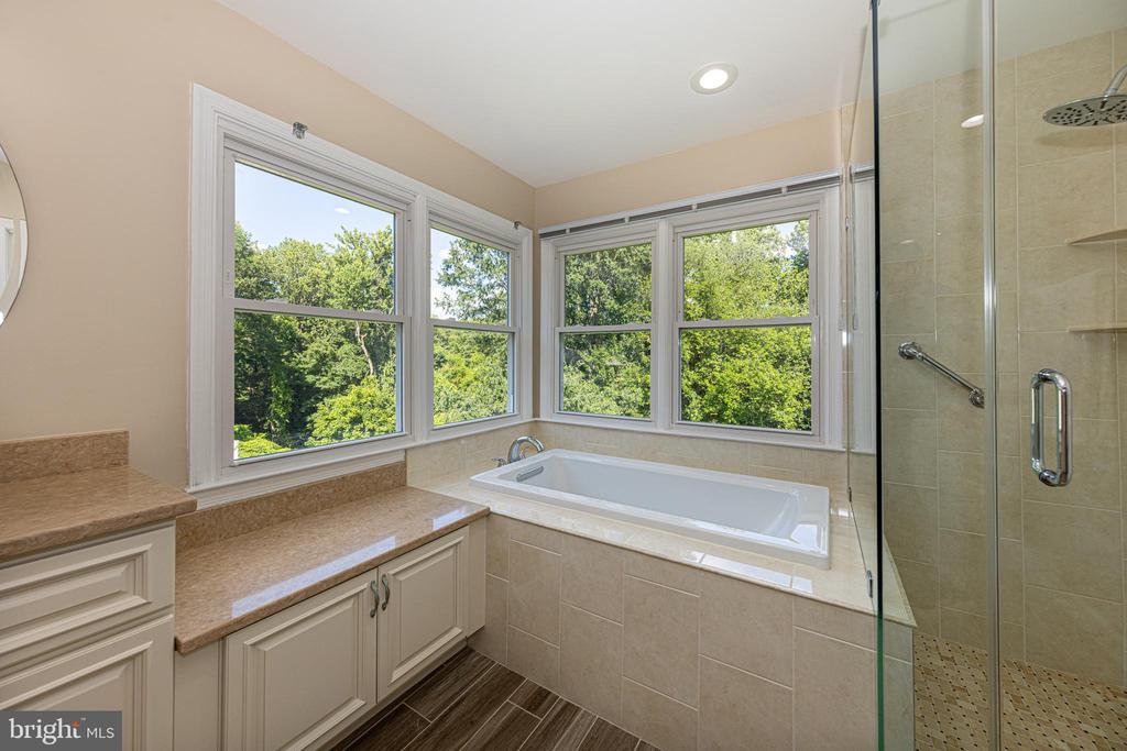 Bathroom with a soaking tub beneath large windows overlooking trees and a glass-enclosed shower.