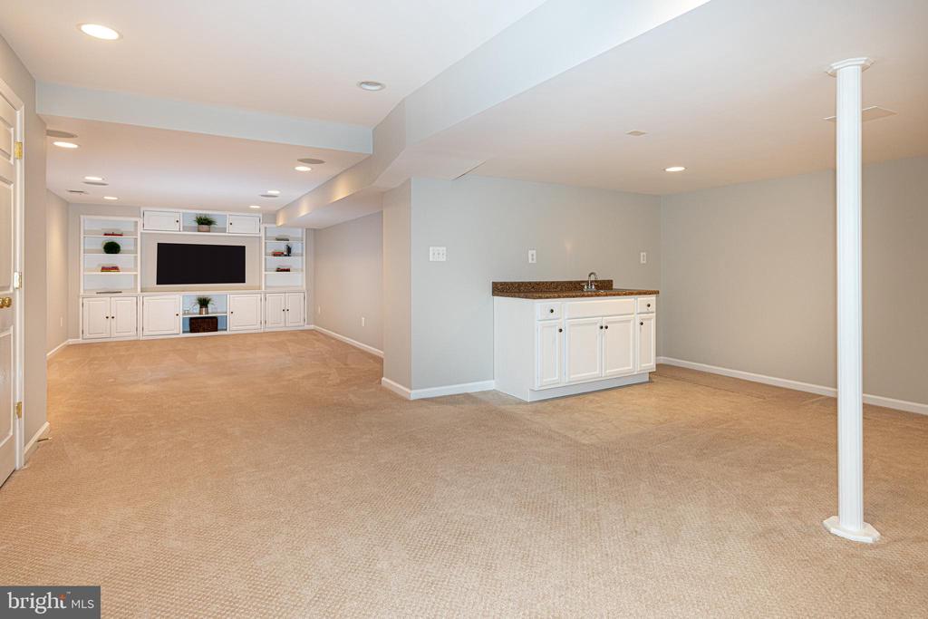 Finished basement recreation room with built-in media cabinetry, wet bar, and beige carpet.