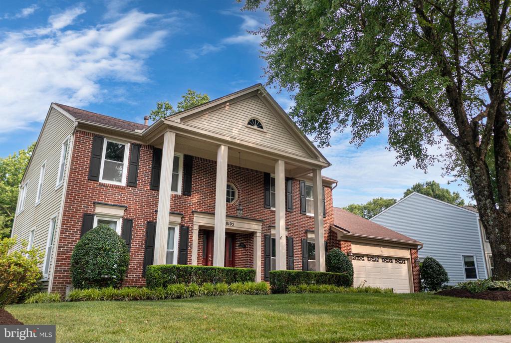 Two-story brick house with a columned entrance, attached garage, and large shade tree.
