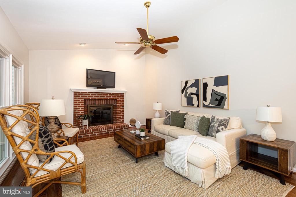 Staged living room with a brick fireplace, cream sofa, wicker chairs, and ceiling fan.