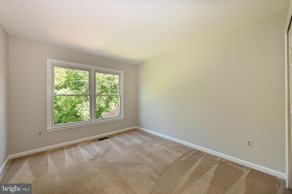 Empty bedroom with tan carpet and a double window overlooking leafy trees.